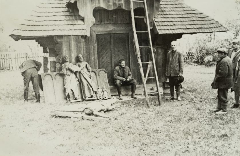 Група осіб на тлі дерев’яної споруди — невідомий